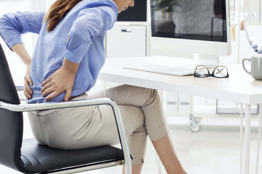 A woman at sitting at her office chair, who seems to be suffering from lower back pain.